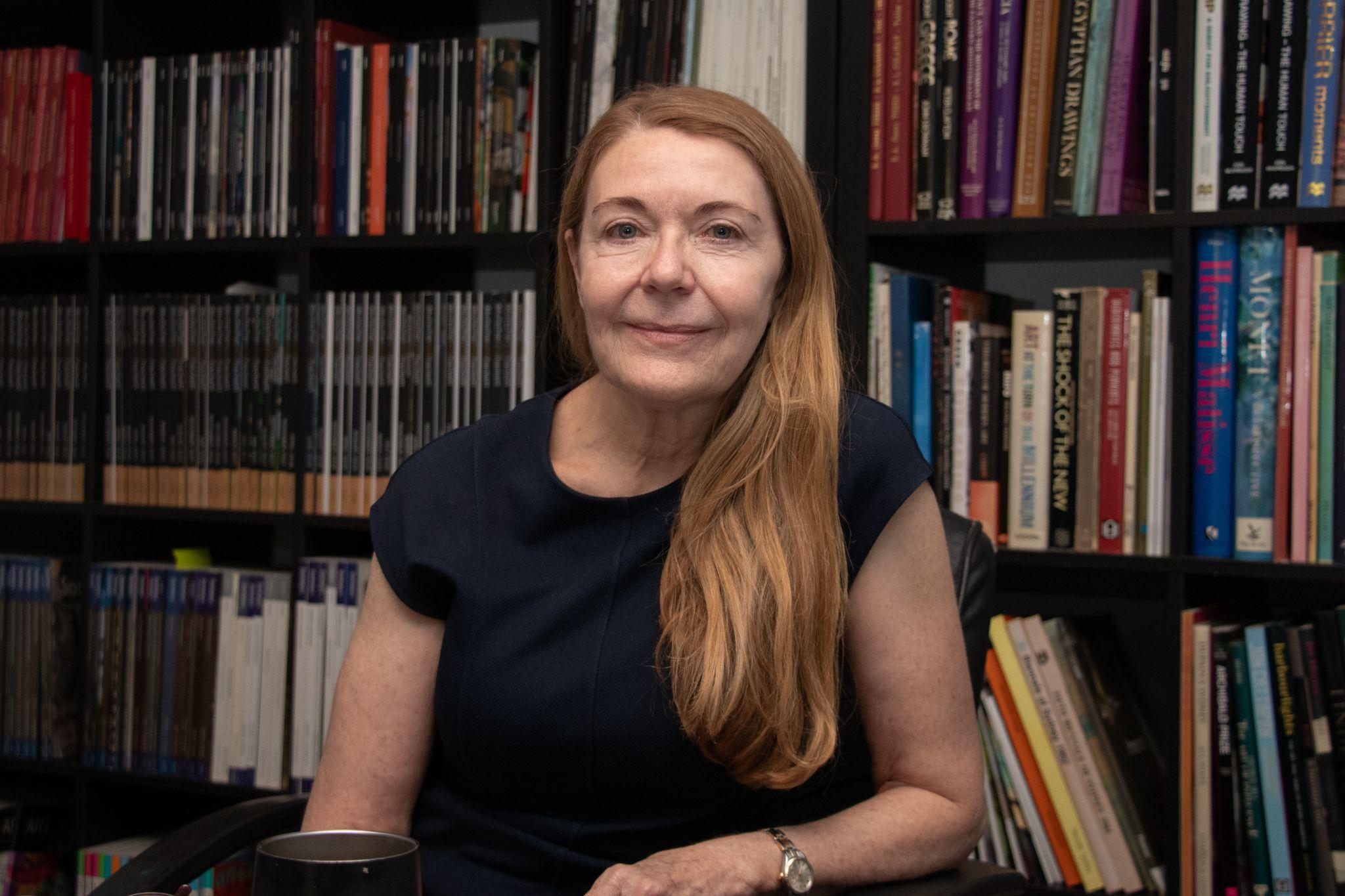 Brenda sitting in her Redfern gallery office in front of hundreds of art history books and auction catalogues. Photograph: Orlando Sagar